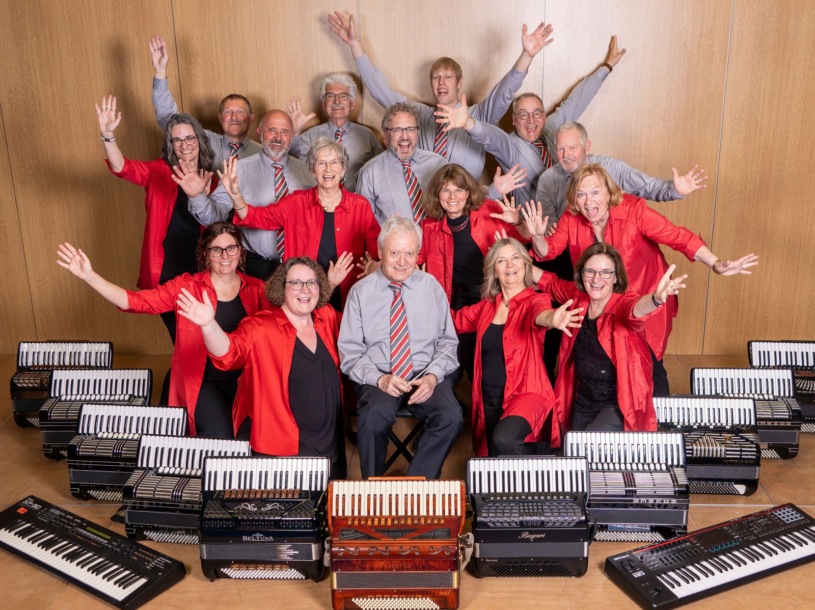 Gruppenfoto des Akkordeonorchesters Rupertigau 2026: die Musikerinnen in roten Blusen, die Musiker in grauen Hemden mit gestreiften Krawatten, davor Akkordeons und Keyboards
